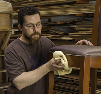 Artist polishing a chair he crafted in a woodworking shop.