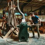 Artist using a machine on a piece of wood in a woodworking workshop.