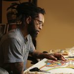 Male artist at a craft table working on a colorful bead project.