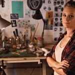 An artist in her workshop, with a desk of art supplies in the background