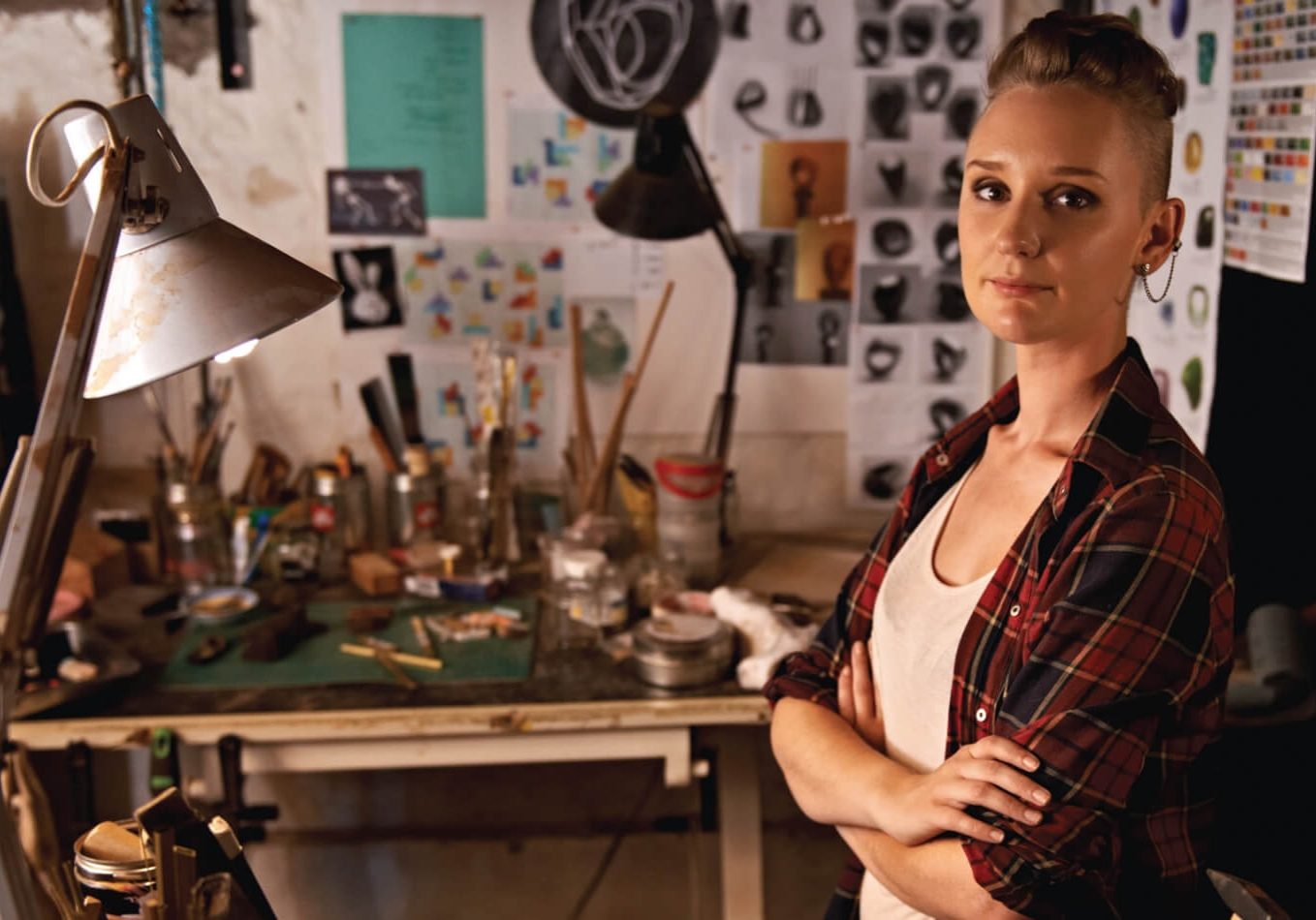 An artist in her workshop, with a desk of art supplies in the background